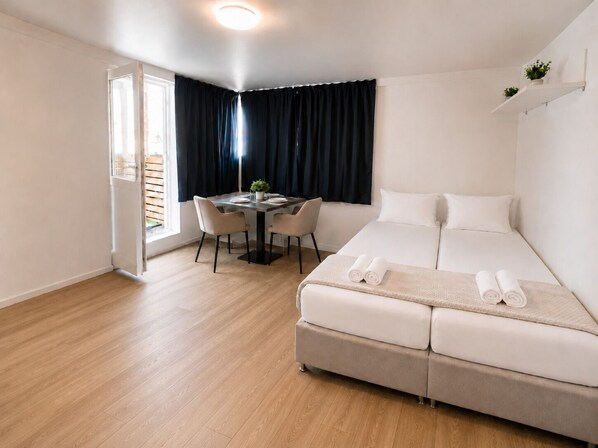 Una habitación de hotel moderna con cama, una mesa de comedor con sillas, una pequeña planta en maceta y una ventana con cortinas.