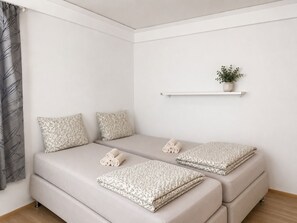Un dormitorio minimalista con cama, dos almohadas, una mesita de noche, una planta y una ventana con cortina.