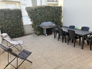 Een terras met een tafel, stoelen, een barbecue en een overdekte parasol.