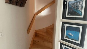 Eine HolztTreppe mit Holzwurf, einem an der Wand montierten Lichtschalter und einer Reihe gerahmter Fotografien mit Küstenansichten.