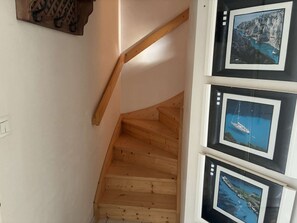 Eine HolztTreppe mit Holzwurf, einem an der Wand montierten Lichtschalter und einer Reihe gerahmter Fotografien mit Küstenansichten.