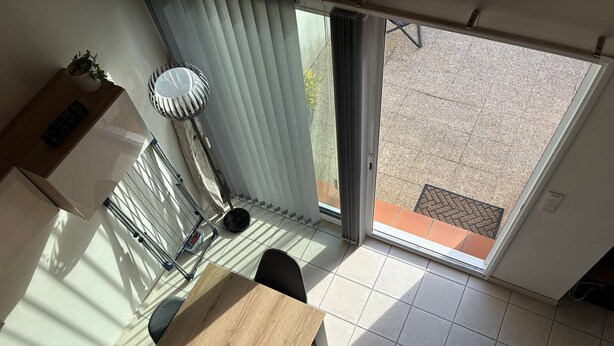 Ein Essbereich mit Tisch, Stühlen, einer Topfpflanze und Blick durch eine Schiebetür auf eine Terrasse.