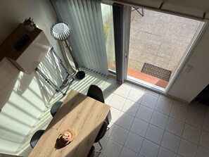 Een eethoek met een tafel, stoelen, een kamerplant en uitzicht door een schuifdeur op een terras.