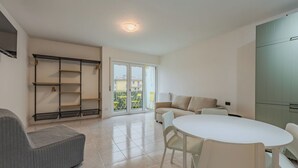 Ein modernes Wohnzimmer mit einer Couch, einem Esstisch mit Stühlen, einer integrierten Regaleinheit und einer Glasschiebetür, die auf einen Balkon führt.