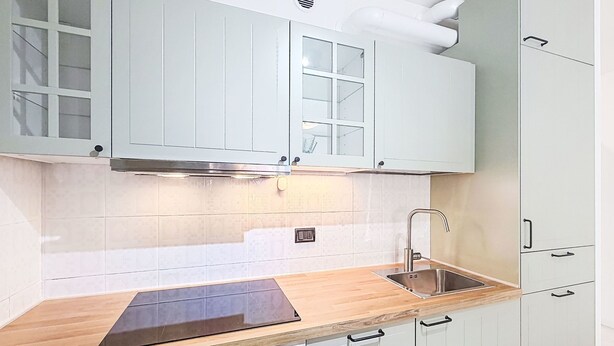 Eine Küche mit weißen Schränken, einer Edelstahl-Spüle, einer Holz Arbeitsplatte und einem eingebauten Backofen.