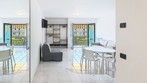 Ein modernes Wohnzimmer mit einer Couch, einem Esstisch und Stühlen. Es gibt eine Einbauschränke mit hängenden Gegenständen.