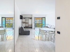 A modern living room with a sofa, a dining table, and chairs. There is a built-in shelving unit with hanging items. - Apartment Nala by Interhome (Riva del Garda)
