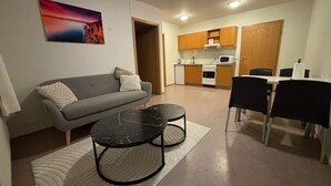 A compact living space with a sofa, two round tables, a dining table with chairs, a kitchen area, and a painting on the wall. - Kosy 1-bedroom apartment in enjoyable Hólar for your stay (Hólar)