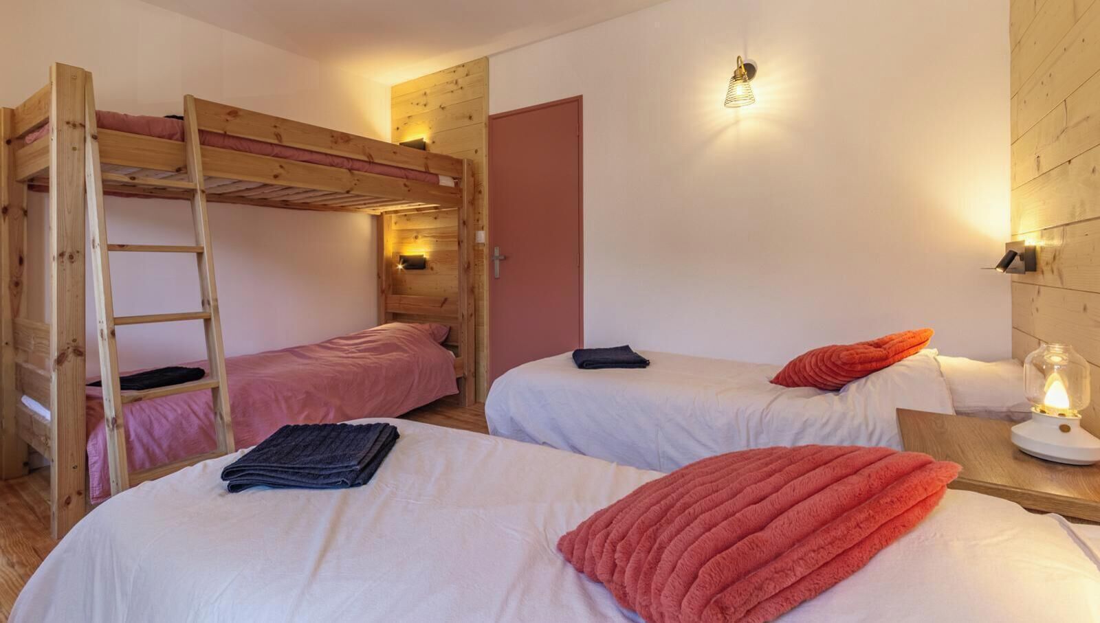 Un dormitorio con literas, dos camas individuales, una escalera, una lámpara de noche y una pared de madera.