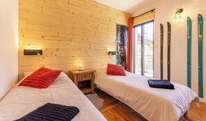 Ein Zimmer mit zwei Betten, Holzwänden, einem Fenster mit Vorhängen, einem Nachttisch mit Lampe und Skiern an der Wand.