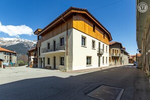 Un edificio de dos pisos con balcón, fachada de madera y montañas al fondo.