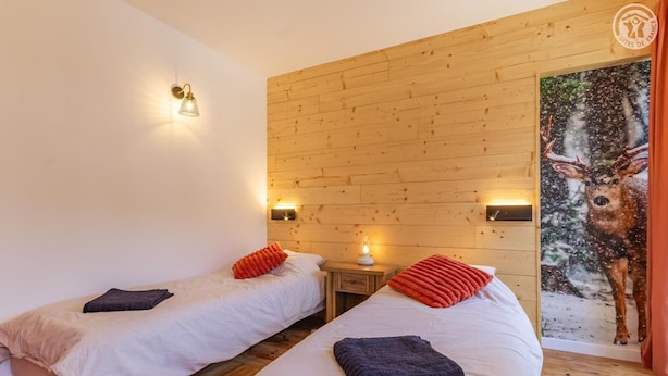 A room with two beds, wooden panel walls, a nightstand with a lamp, and a deer painting. - Le Jovet - AIME LA PLAGNE (AIME LA PLAGNE)