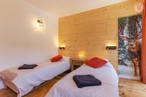 A room with two beds, wooden panel walls, a nightstand with a lamp, and a deer painting. - Le Jovet - AIME LA PLAGNE (AIME LA PLAGNE)