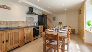 A kitchen with wooden cabinets, a black oven, and a dining table set for four. - Le Jovet - AIME LA PLAGNE (AIME LA PLAGNE)