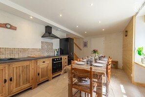 Una cocina moderna con armarios de madera, un horno negro y un comedor con una mesa preparada para cuatro.