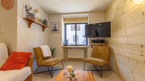 A cozy living room with a sofa, two armchairs, a coffee table with a vase, a TV mounted on the wall, and a window with a view. - Le Jovet - AIME LA PLAGNE (AIME LA PLAGNE)