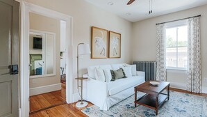 A living room with a white sofa, a coffee table, a floor lamp, and two framed pictures on the wall. - Red Bud Suite (Staunton)