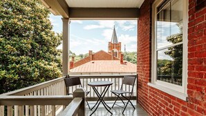 A balcony with a view of a church steeple, a brick building, and a wooden railing. - Red Bud Suite (Staunton)