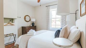 A bedroom with a bed, a bedside table, a hanging light, a ceiling fan, a window with curtains, and a wall-mounted mirror.