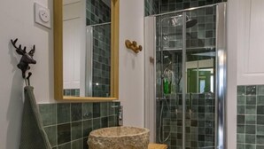 Ein Badezimmer mit Waschtisch aus Holz, einem Becken aus Stein, einem Spiegel, einer Dusche mit Glastüren und einem Handtuchhalter mit Dekoration im Hirschgeweih-Stil.