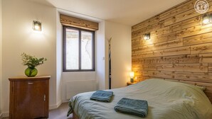 Ein Schlafzimmer mit einem Holzkopfteil, einem Fenster mit Jalousien, einer Nachttischlampe und einer grünen Tagesdecke.