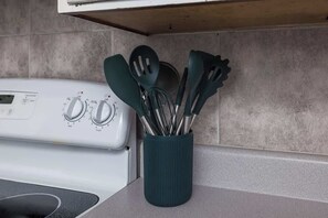 A kitchen with a white stove, a teal utensil holder, and a tiled backsplash.