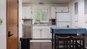 Una cucina moderna con mobili bianchi, un frigorifero in acciaio inossidabile, una macchina da caffè e un'area pranzo con tovaglia blu e sgabelli.