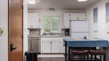 A modern kitchen with white cabinets, a stainless steel refrigerator, a coffee maker, and a dining area with a blue tablecloth and stools.