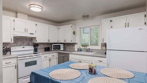 Una cucina con mobili bianchi, un fornello, un forno a microonde e un frigorifero.
