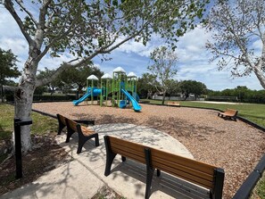 Ein Spielplatz mit Rutschen und Klettergerüsten, umgeben von Bänken und Bäumen.