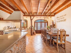 A spacious kitchen with a stone island, wooden beams, and a dining area with a large table and chairs. - Son Aloy by Interhome (Búger)