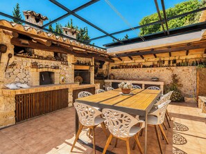 Eine Terrasse im Freien mit Kamin aus Stein, Holztisch und Stühlen.