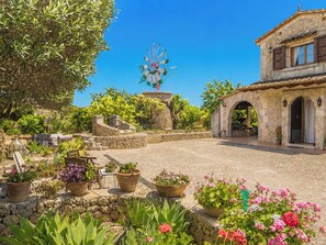 A courtyard with stone walls, potted plants, a windmill, and a building with arches. - Son Aloy by Interhome (Búger)