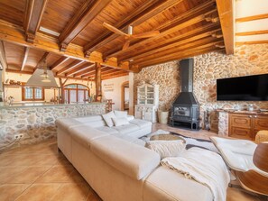 A cozy living room with a stone wall, wooden ceiling beams, a large sofa, a fireplace, and a television. - Son Aloy by Interhome (Búger)
