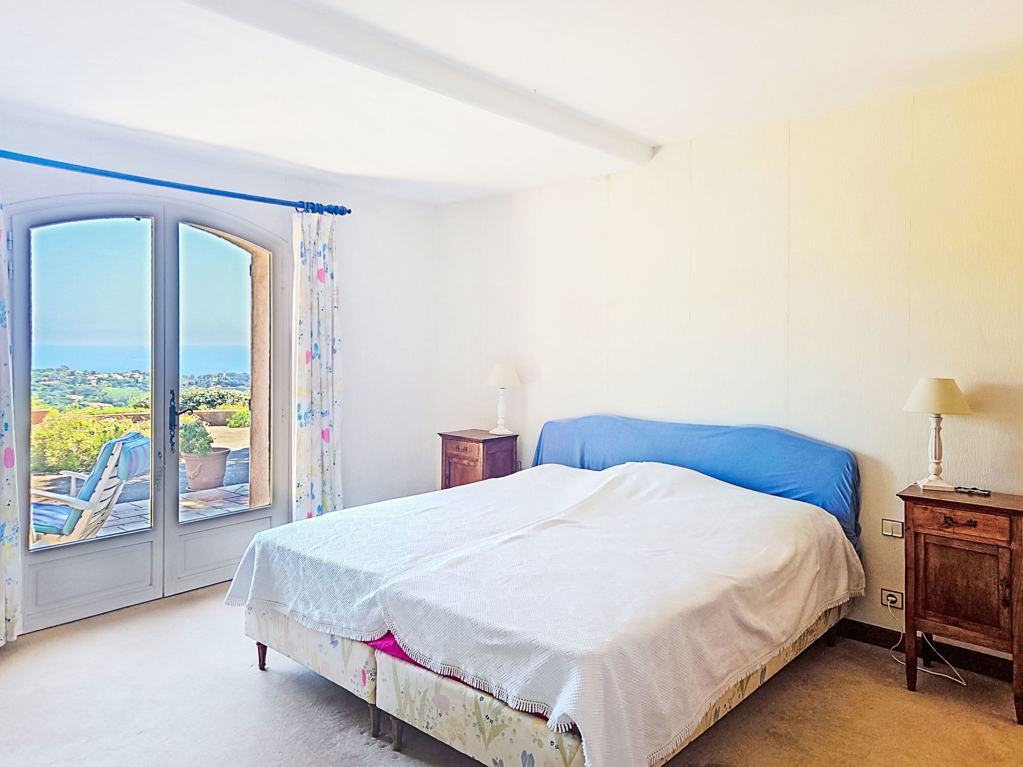 A bedroom with a bed, a nightstand, a window with a view, and a door.