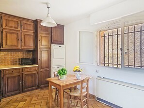 Een keuken met houten kastjes, een witte koelkast, een eettafel met stoelen en een raam met metalen tralies.
