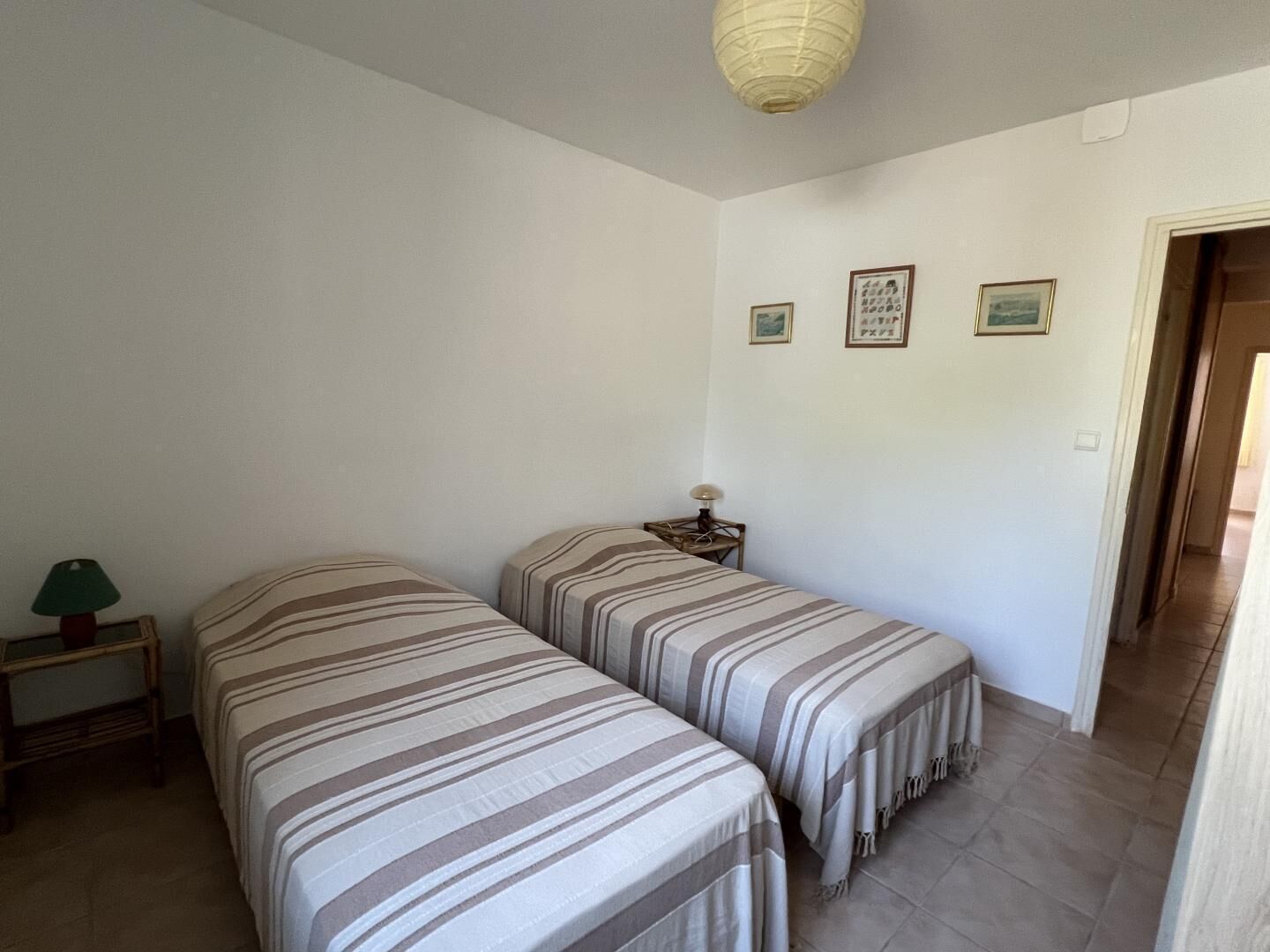 A room with two beds, a nightstand with a lamp, and a door leading to another room.