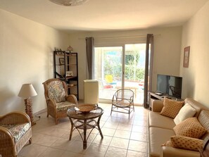 Ein Wohnzimmer mit einer Couch, zwei Korbstühlen, einem kleinen runden Tisch, einem Fernseher und einem Bücherregal.