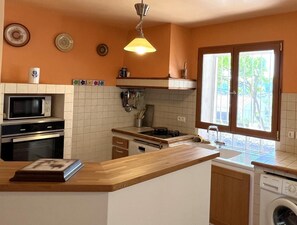 Eine Küche mit Mikrowelle, Backofen, Spüle und einem Fenster mit Blick auf Grünflächen.
