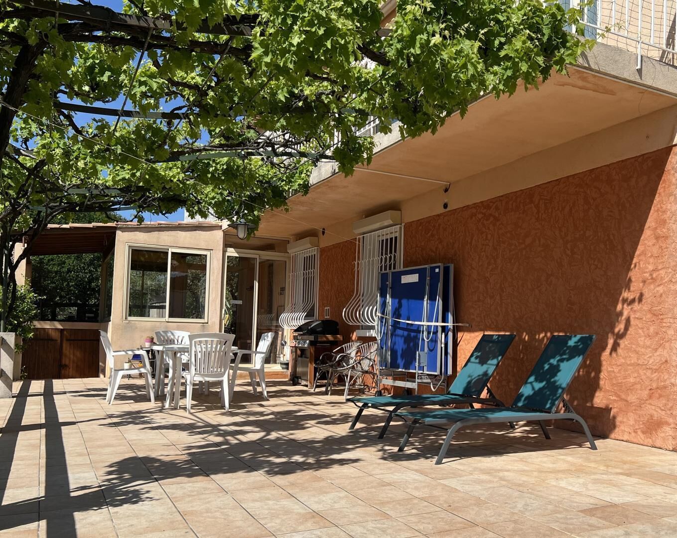 Une terrasse extérieure avec une table et des chaises, un barbecue et un espace abrité agrémenté d’une pergola.
