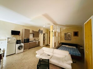 Un espacio habitable pequeño con kitchenette, un sofá, una cama y una lavadora.