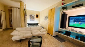 Ein Wohnzimmer mit einer Couch, einem Glastisch, einem Fernseher und einem Holzschrank.