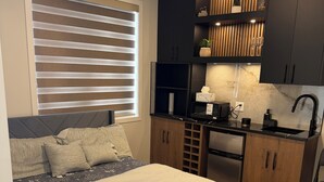 Un dormitorio moderno con cama, escritorio empotrado, mueble de madera oscura y ventana con persianas.