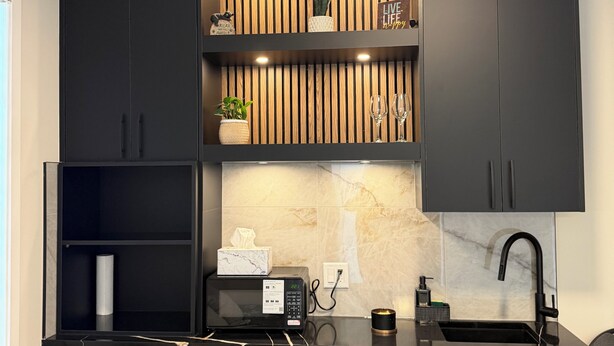 Una cocina compacta con gabinetes negros, microondas integrado, un lavamanos y un esparcidor para copas de vino.
