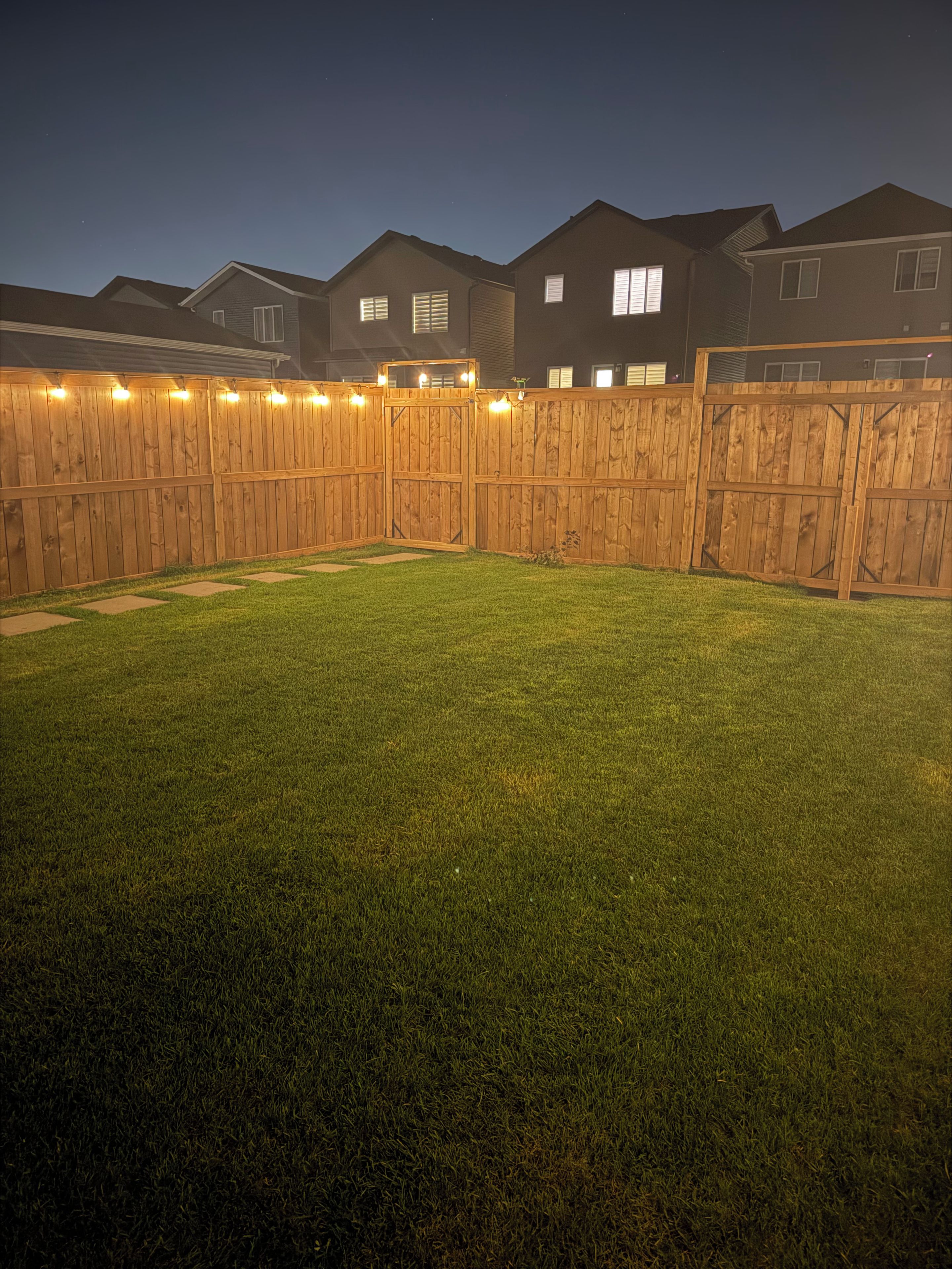 A backyard with a wooden fence, a well-maintained lawn, and houses in the background.