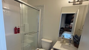 Un baño moderno con cabina de ducha de vidrio, inodoro, lavamanos con tocador y espejo sobre el lavamanos.