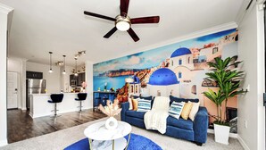 A modern living room with a blue sofa, a white coffee table, and a kitchen in the background. - Santorini - 2Bedroom/2Bath/NRG Stadium/Medical Center/Pool/Gym/Sleeps 6 (Houston)