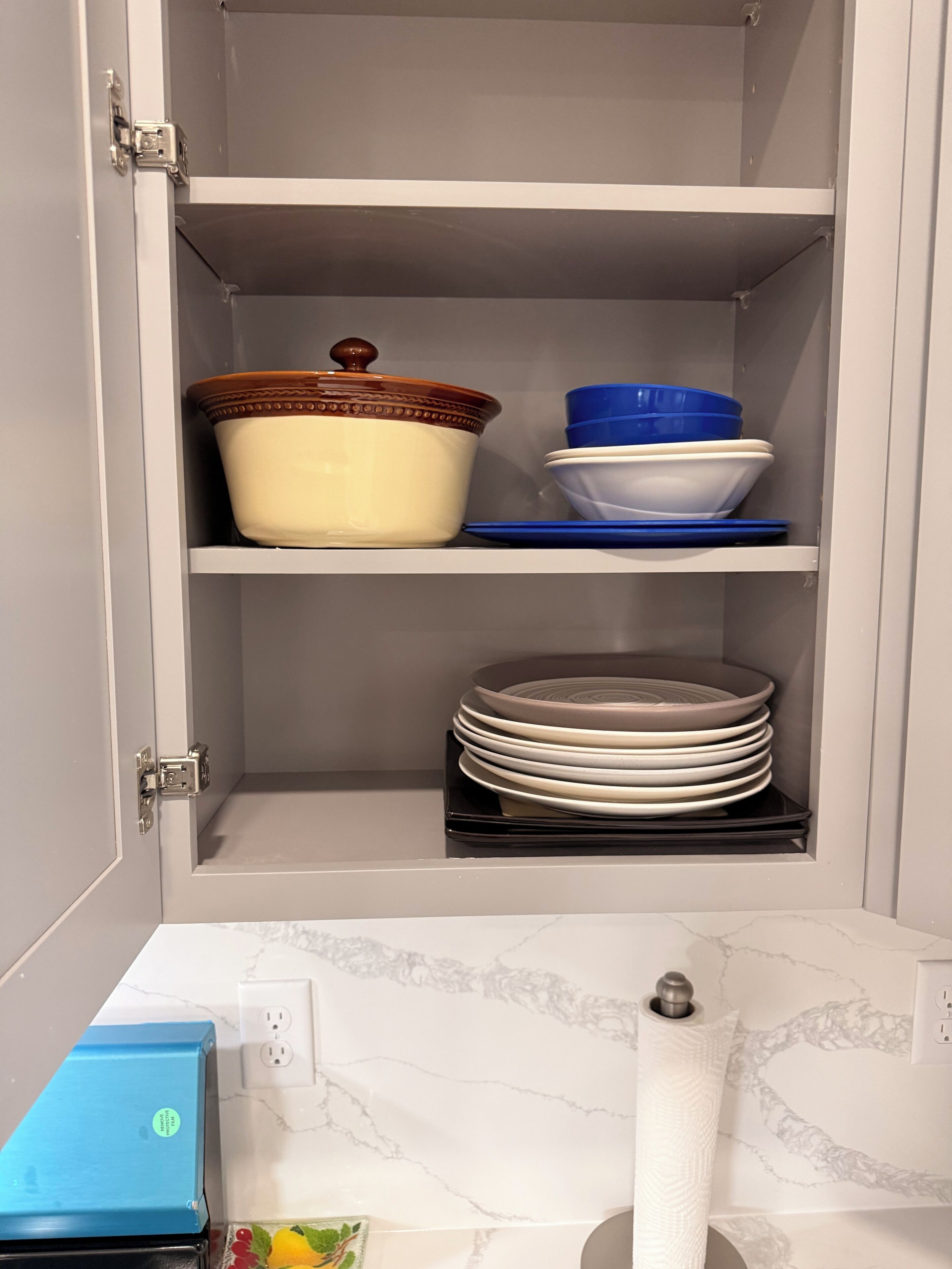 Un mueble de cocina con una caja azul, un dispensador de toallas de papel blanco y una encimera de mármol.