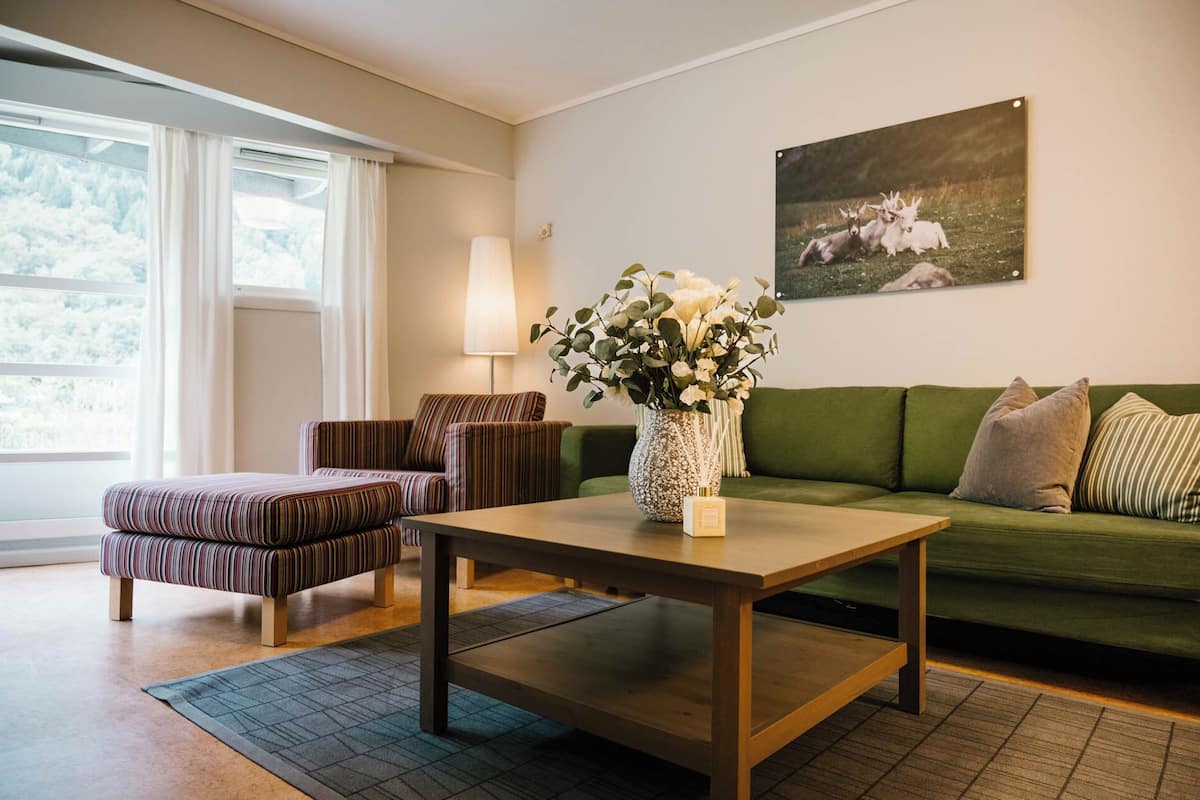 Una sala de estar con un sofá verde, un sillón a rayas y una mesa de centro con un jarrón de flores.