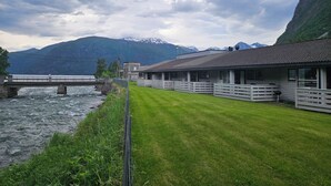 A riverside hotel with a bridge, a grassy lawn, and mountains in the background. - Norddalstunet (Norddal)